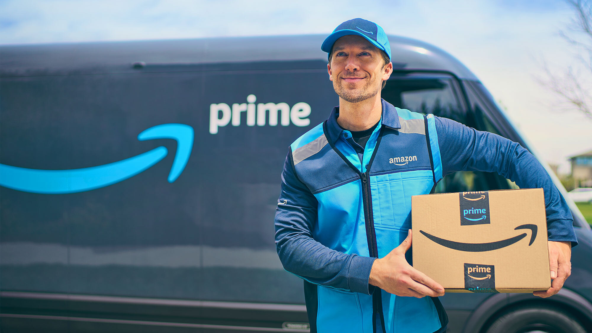 Corriere Amazon che consegna un pacco. Sullo sfondo si intravede un furgone.