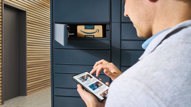 Cliente con in mano uno smartphone ritira un pacco Amazon dall’armadietto del locker.